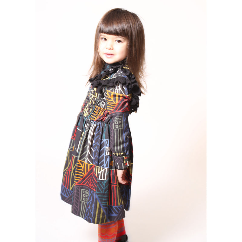 Girl wearing a flared long sleeve frock in this season's Normanz print on soft corduroy features black color smocking at the bodice, Multicolour, Tia Cibani.