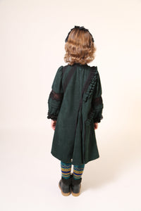 Girl wearing a party dress in soft Liquid Canvas fabric with diagonal ruffle details. Lace trim and ribbon at ruffles, neckline, elbows, and cuffs. Mock collar with button closure and invisible zipper at back. Big A-flare sweep at godet panels, cinched long sleeves with fold-up details. Colour: Celtic,Tia Cibani.