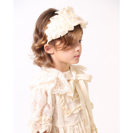 Girl wearing Tiara headband crafted with taffeta base, pleated lace trim at crown, and hand-stitched pearls, white, Tia Cibani.