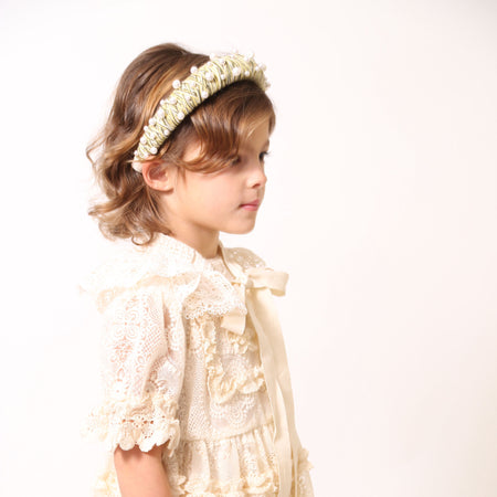 Child wearing a headband covered in mustard yellow and white thread with various pearls attached, by Tia Cibani.