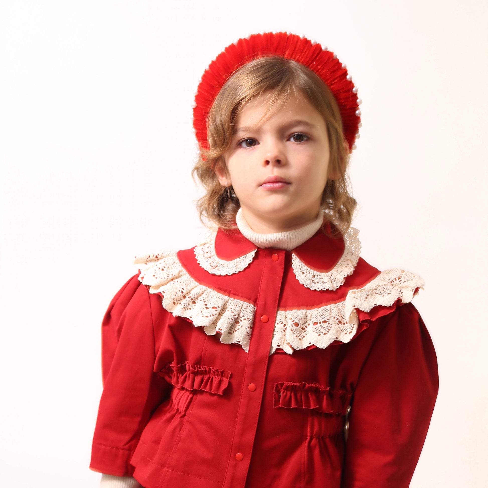 Girl wearing an Oversized headband crafted with playful pipe cleaners, finished with delicately placed pearls at the crown. Colour: Rouge, Tia Cibani.