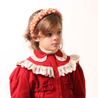 Child wearing a headband covered in red and yellow thread with various pearls attached, by Tia Cibani.