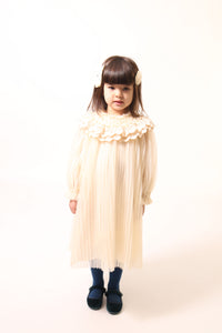 Girl wearing Tealength Argyle Tulle frock with pearls and stretch tonal smocking at neck and sleeve cuffs. Lace pleated and ruffled collar, high crew neckline, hidden zipper at center back. Lined body with cotton lining, unlined sleeves for airy feel. Three layers of tulle with raw edge. Colour: Opal, Tia Cibani.