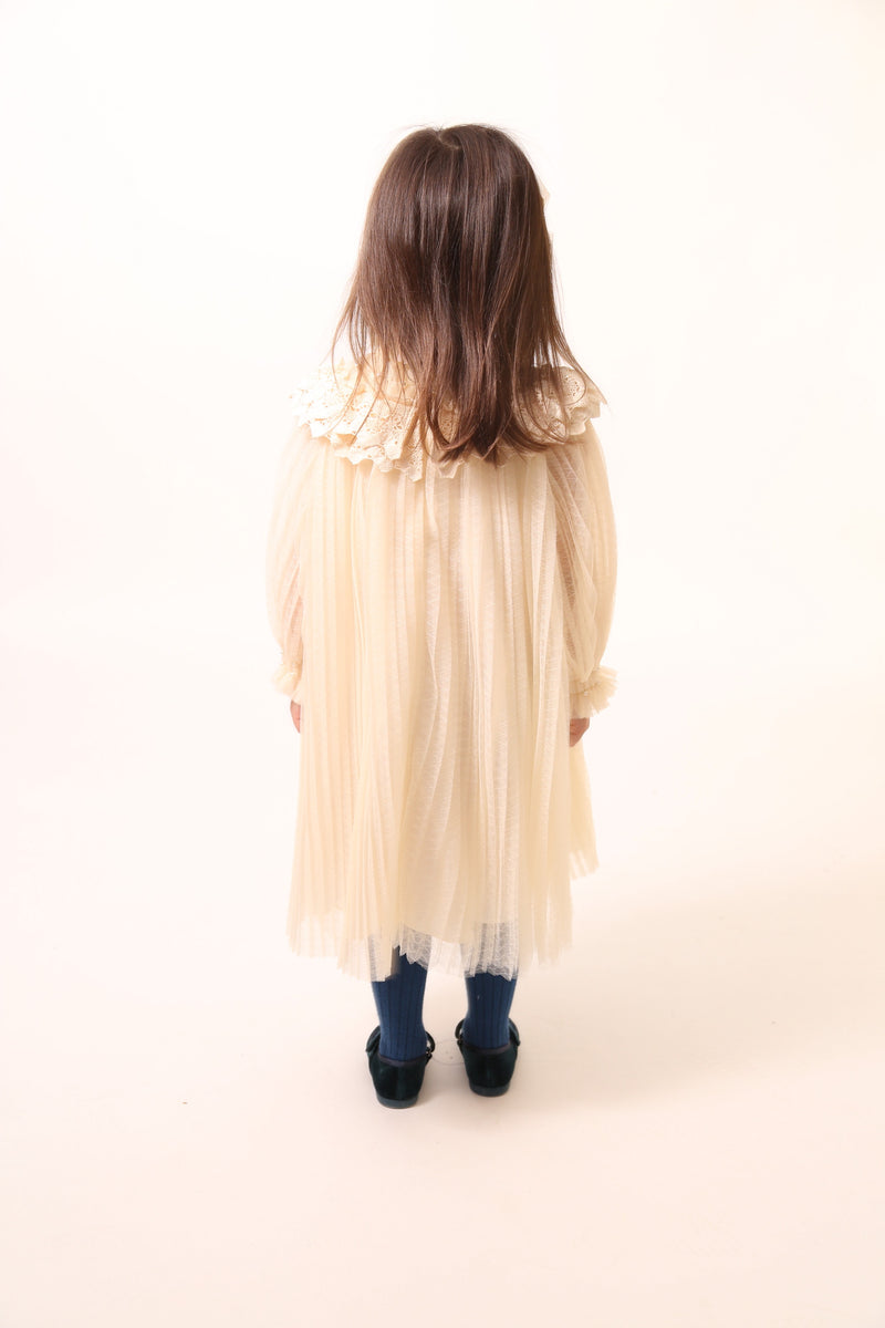 Girl wearing Tealength Argyle Tulle frock with pearls and stretch tonal smocking at neck and sleeve cuffs. Lace pleated and ruffled collar, high crew neckline, hidden zipper at center back. Lined body with cotton lining, unlined sleeves for airy feel. Three layers of tulle with raw edge. Colour: Opal, Tia Cibani.