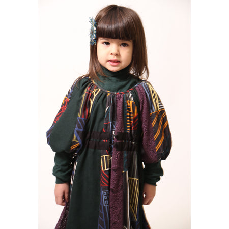 Girl wearing Patchworked frock for girls with signature print, embroidered lace, and liquid canvas fabric. Soft cotton lining, layered Argyle Tulle for volume, cinched sleeves, scoop neckline, and adjustable ribbon waist detail. Perfect for special occasions. Dark Rainbow,Tia Cibani.
