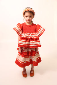 Girl wearing a top in luxurious Taffeta with elasticized smocking at neckline, ruffle detail, and embroidered lace trim and ribbon at body and flutter sleeves. Tonal ribbon ties at the back of the neck. Unlined for lightweight feel. Colour: Rouge and white, Tia Cibani. / A girl wearing Tealength two-tiered taffeta skirt with elasticized smocking at the waistband, embroidered lace trim, and ribbon at each tier. Unlined for lightweight feel. Colour: Rouge and White, Tia Cibani.