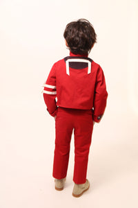 Boy wearing a bold and stylish Malok Military Jacket for boys, inspired by traditional military dress. Patchworked with cotton twill and velvet accents. Features zip welt pockets, yoke at back, snap tabs at sleeves, and double-breasted snap closure for comfort and charm. Relaxed box fit for easy layering. Textured structured ribbon details on front and sleeves with free-hanging tassels for contemporary flair. Scoop hem, stand-up collar. Perfect with Malok Slim Fit Trousers. Rouge, Tia Cibani.