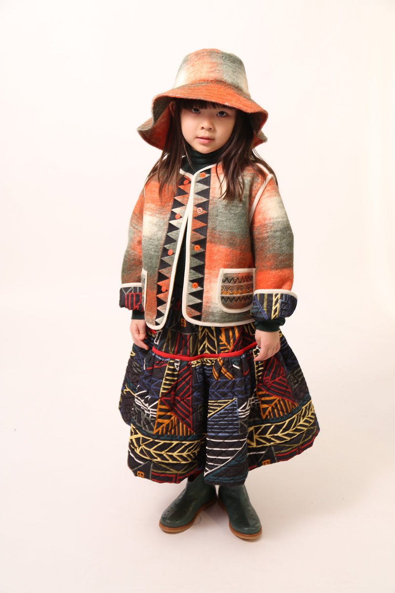 Girl wearing a rainbow printed voluminous skirt features diamond harlequin pattern tufting and padded design, Tia Cibani.