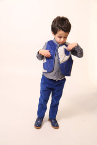 Boy wearing slim-fitting trousers in structured velvet, featuring subtle patchwork at hips and pocket flaps. Includes functional snaps, elastic waistband with adjustable button and loop, and zip-fly with hook and eye closure. Made from 99% Cotton, 1% Elastane with 100% Cotton lining. Color: Blue.