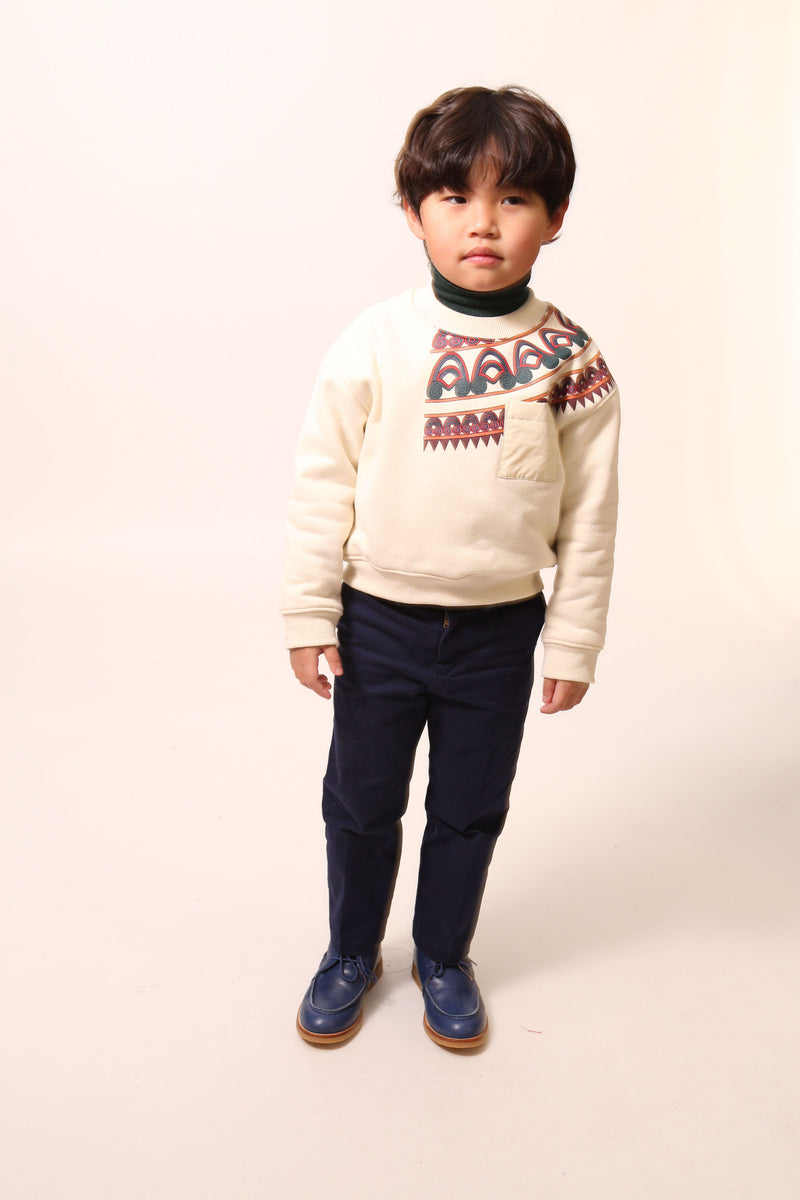 Boy wearing Sueded Fleece jersey pullover for boys, featuring long sleeves, tonal jersey ribbing at neckline, hem, and cuffs for comfort and style. Colorful asymmetric screen print at shoulder. Taffeta pocket detail at left chest for treasures. Dropped shoulders, relaxed fit. White, Tia Cibani.