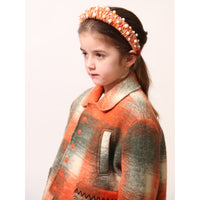 Girl wearing Loden style jacket in cozy Celtic Shadow Plaid, padded and lined for warmth. Snap closure, boxy yet tailored fit with sharp collar, roomy front pockets, and embroidery design at sleeve cuffs. Colour: Multicolour, mainly orange, Tia Cibani.