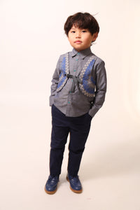 Boy wearing a western-inspired take on classic boy's button-up with scoop high-low hem for modern twist. Built-in vest with two-toned embroidery design and textured ribbons at overlay. Snap closure at center front for easy dressing. Perfect for any occasion, from family gatherings to formal events. Cotton. Blue, Tia Cibani. 