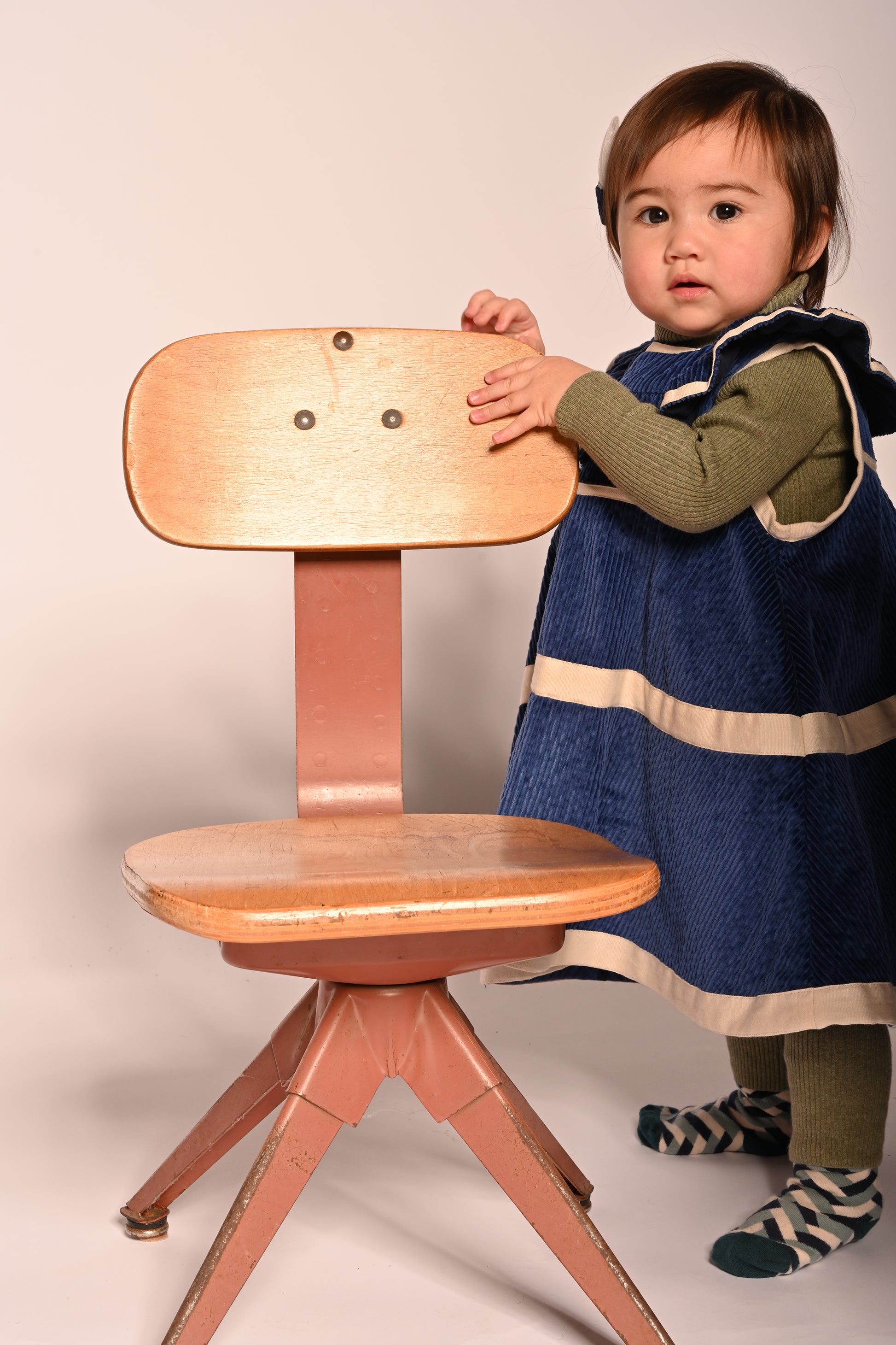 baby girl wearing corduroy blue dress with white ribbon stripes going across