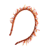 Headband wrapped in multi-colored, predominantly orange, wool yarn, with fringing at the crown and hand-stitched pearls at the top, by Tia Cibani.