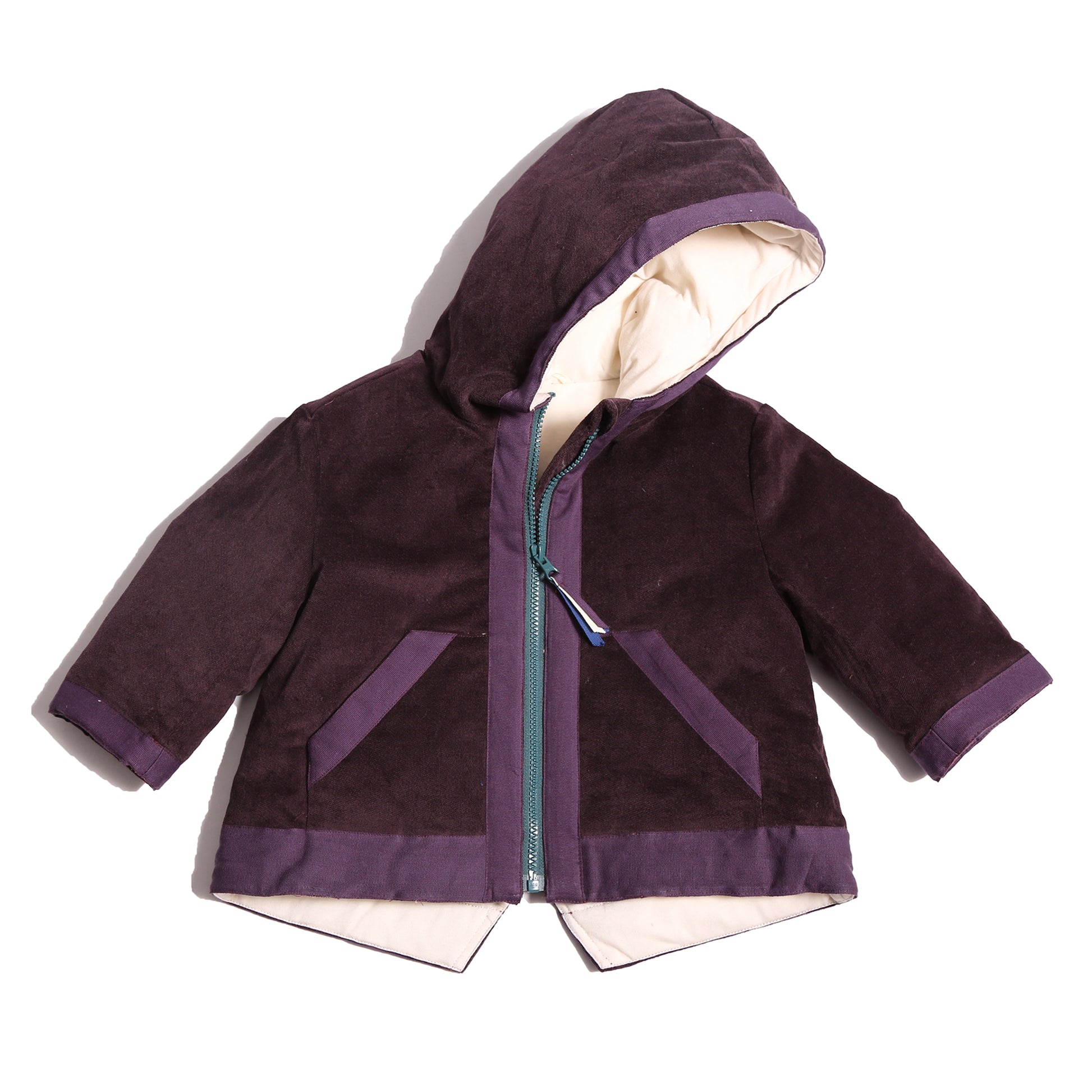 Baby coat made from Prune Breton Tarp Velvet, featuring down filling, an attached hood, slanted ribbon welt pockets, a V cut-out vent at the back hemline, and a center front zipper with a multi-colored ribbon pully for added flair. Lined with soft jersey at the body and nylon lining in the sleeves, by Tia Cibani.