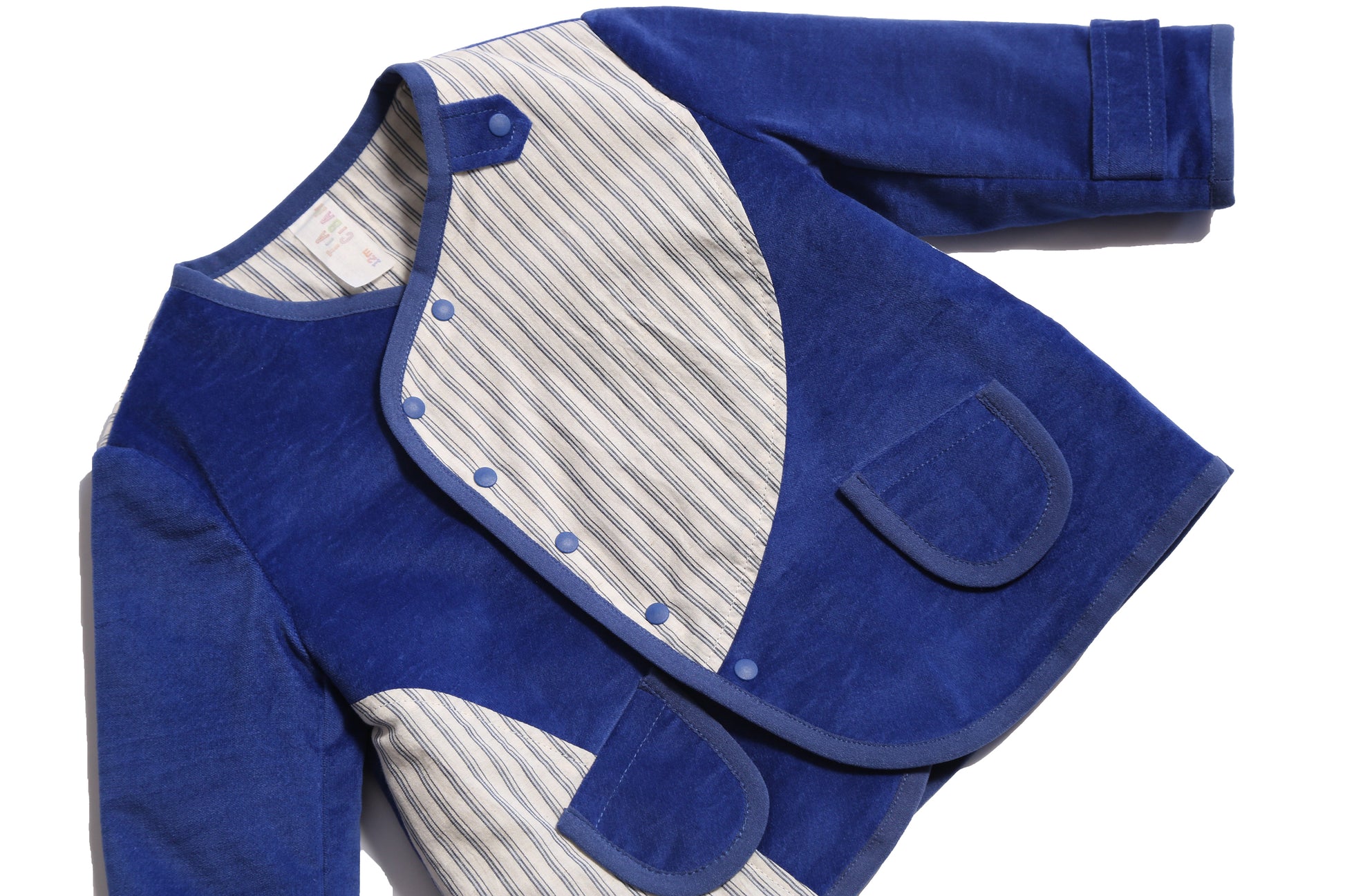 Padded patchwork jacket in Blue and White, featuring an easy relaxed fit for comfort and layering. Includes a snap placket closure at the front flap for a touch of military-inspired flair. Made from structured velvet and soft cotton striped shirting, fully faced for comfort. Complete with patch pockets, interior ribbon tie, and binding tape trim throughout, ideal for all-day wear, by Tia Cibani. Detail.