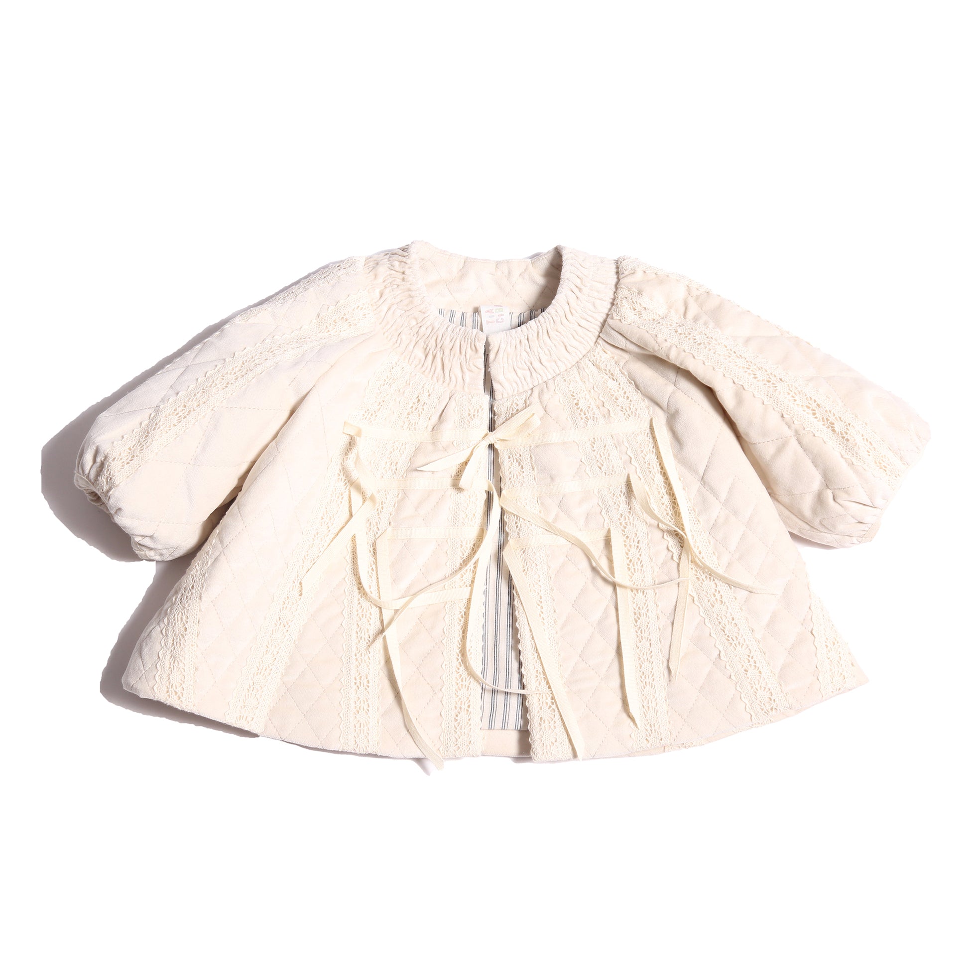 Adorable baby girl jacket in Opal color, featuring lace trim appliqué throughout and tonal intricate smocking at the neckline. Lightly padded for warmth and comfort, with cinched sleeve cuffs and minimal ribbons at the center front for a decorative touch. Lined in soft cotton striped shirting at the body and cire at the sleeves. Perfect for chilly days, by Tia Cibani.