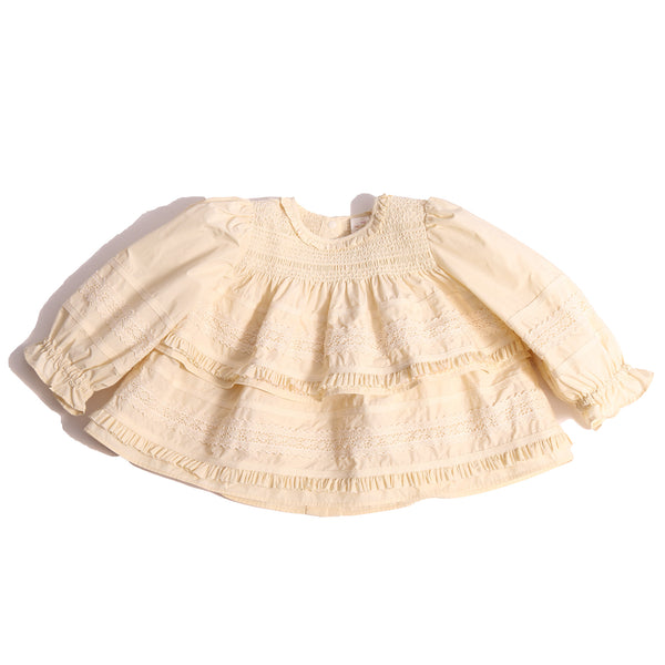 Darling baby smocked blouse in Opal color, made from luxurious Taffeta with delicate lace embroidered ribbon trim throughout. Features tonal elasticized smocking at the neckline, snaps at the back for easy dressing, and cinched long sleeves with elastic cuffs for a snug fit. Adorned with tiers of small ruffles at each lace appliqué, perfect for special occasions, by Tia Cibani.