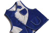  Padded patchwork vest in Blue and White, featuring an easy box fit for layering and comfort. Includes binding tape at all edges, patch pockets for storage, and a snap button closure at the center front flap. Made from structured velvet and soft cotton striped shirting, fully faced for added comfort. Versatile and stylish, perfect for any occasion, by Tia Cibani. Detail.