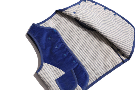  Padded patchwork vest in Blue and White, featuring an easy box fit for layering and comfort. Includes binding tape at all edges, patch pockets for storage, and a snap button closure at the center front flap. Made from structured velvet and soft cotton striped shirting, fully faced for added comfort. Versatile and stylish, perfect for any occasion, by Tia Cibani. Detail.