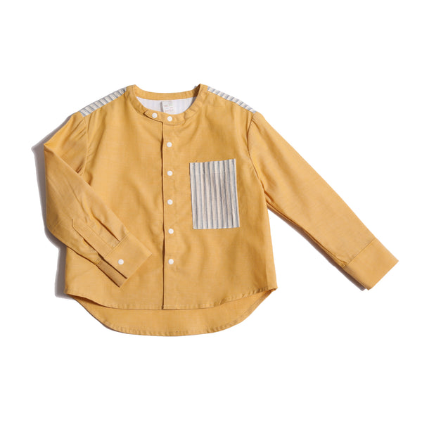 Boy wearing this season's Finn Classic Snap Shirt in patchwork Chambray Cotton Shirting and lightweight striped cotton shirting at pocket and yoke. Snaps at center front and cuffs, high-low scoop hem, long sleeves. Colour: Yellow, Tia Cibani.