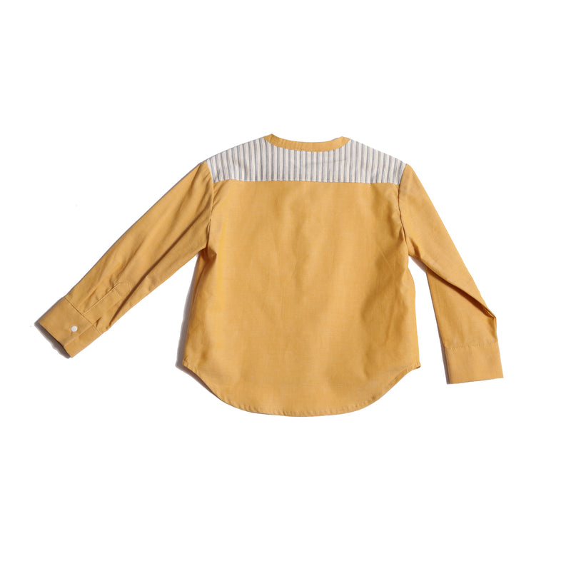 Boy wearing this season's Finn Classic Snap Shirt in patchwork Chambray Cotton Shirting and lightweight striped cotton shirting at pocket and yoke. Snaps at center front and cuffs, high-low scoop hem, long sleeves. Colour: Yellow, Tia Cibani.