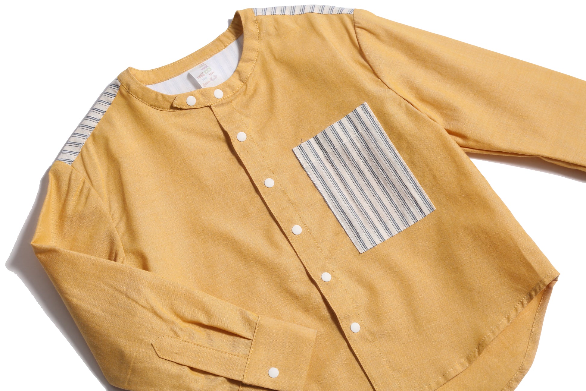 Boy wearing this season's Finn Classic Snap Shirt in patchwork Chambray Cotton Shirting and lightweight striped cotton shirting at pocket and yoke. Snaps at center front and cuffs, high-low scoop hem, long sleeves. Colour: Yellow, Tia Cibani.