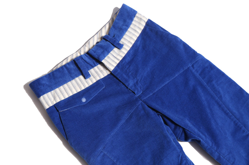 Slim-fitting trousers in structured velvet, featuring subtle patchwork at hips and pocket flaps. Includes functional snaps, elastic waistband with adjustable button and loop, and zip-fly with hook and eye closure. Made from 99% Cotton, 1% Elastane with 100% Cotton lining. Color: Blue.