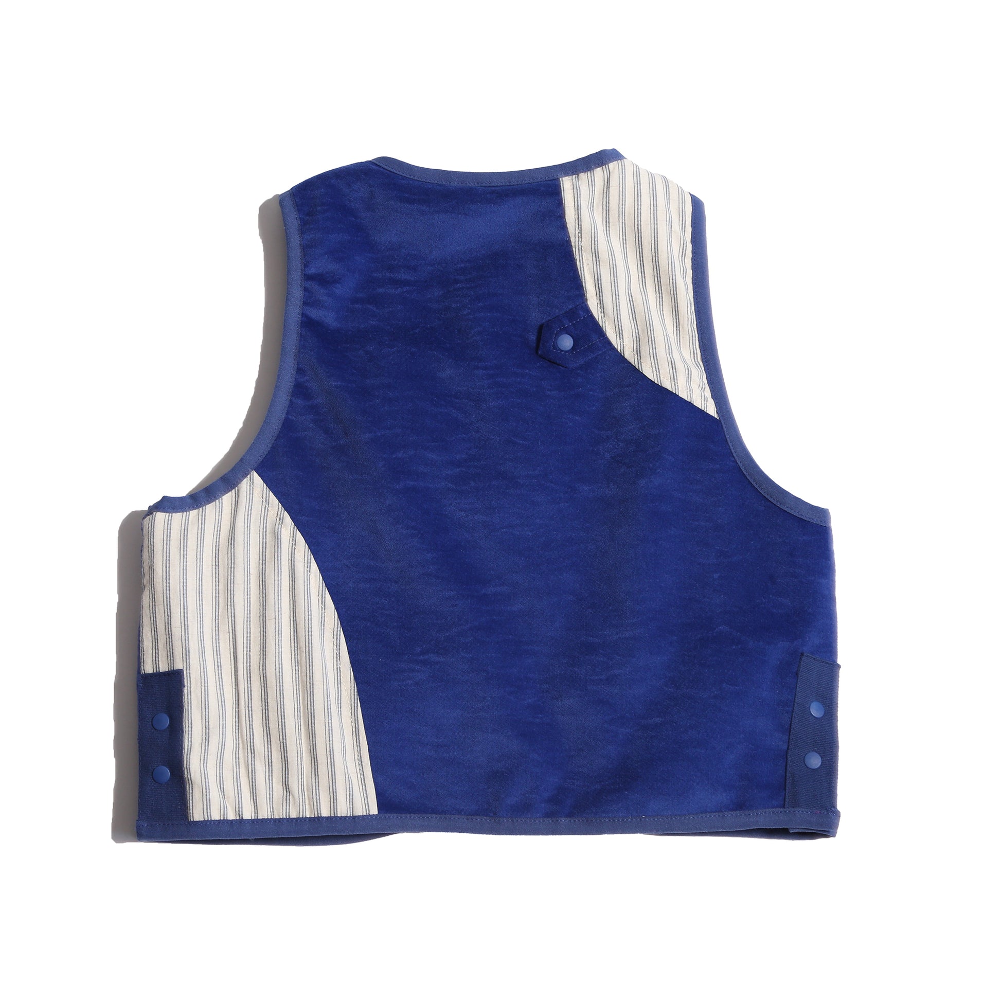 Versatile padded patchwork vest for boys, combining style and comfort with easy box fit for layering. Features binding tape at edges, patch pockets for treasures, and snap button closure at center front flap. Fully faced in cotton striped shirting, patchworked with structured velvet exterior for added fun. Great for formal and casual occasions. Pair with classic boy's button-ups and Breton Slim Fit Trousers for refined look. Blue and white, Tia Cibani.