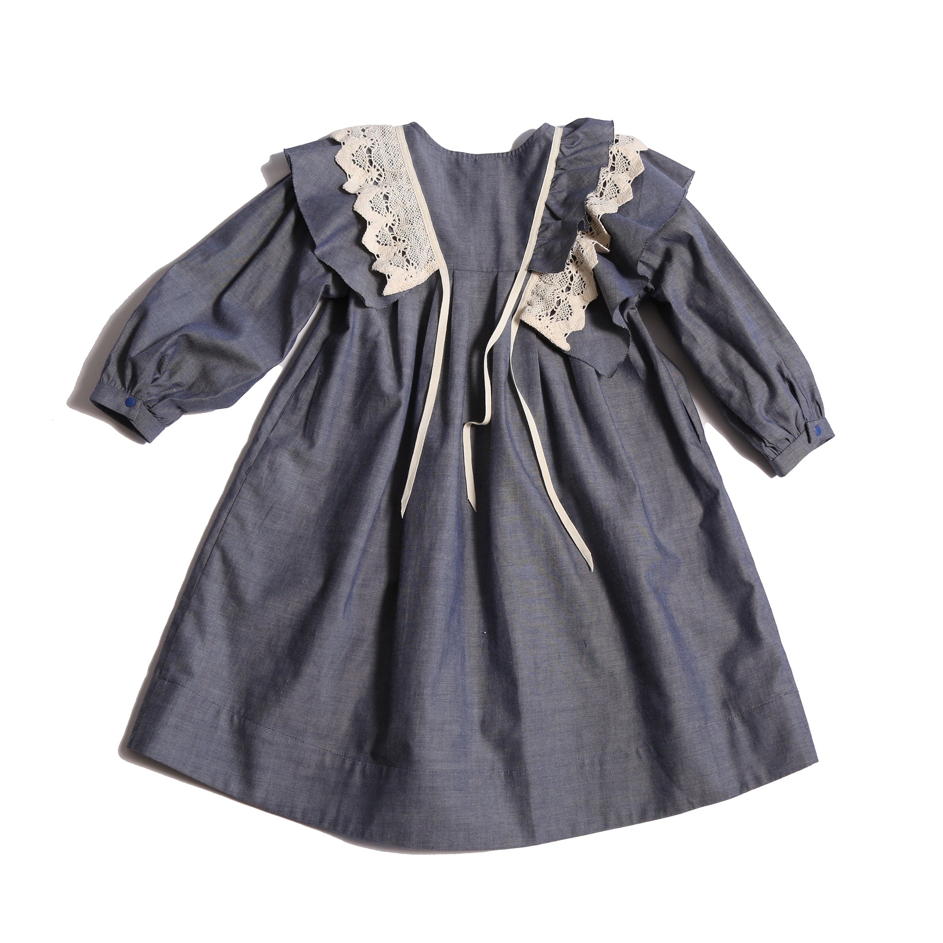 Voluminous dress in unlined Chambray Cotton Shirting with 3-D self ruffles at shoulders and delicate lace ruffles overlay. Decorative ribbons from ruffles. Long cinched sleeves, tealength silhouette, henley snap placket at center front neckline. Colour: Blue, Tia Cibani.