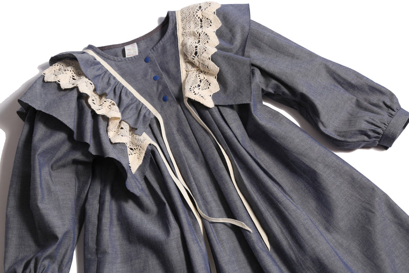 Voluminous dress in unlined Chambray Cotton Shirting with 3-D self ruffles at shoulders and delicate lace ruffles overlay. Decorative ribbons from ruffles. Long cinched sleeves, tealength silhouette, henley snap placket at center front neckline. Colour: Blue, Tia Cibani.