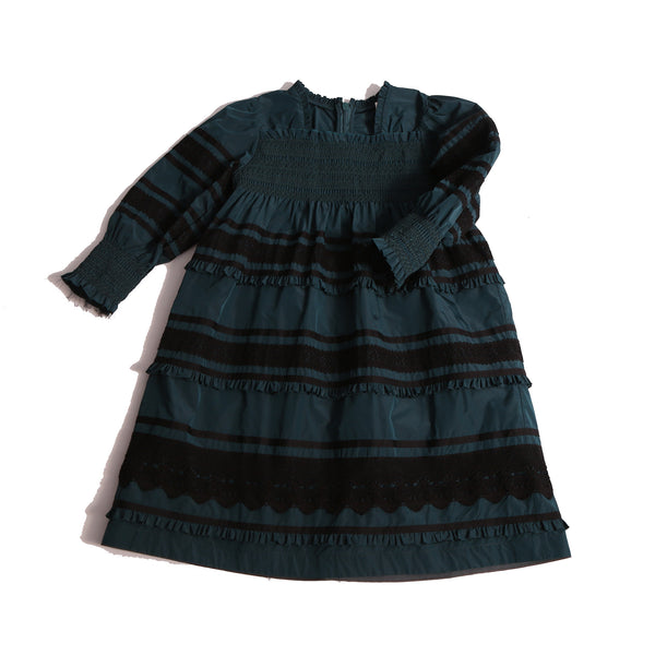 Tealength frock in luxurious Taffeta with elasticized smocking at bust and cuffs, tiers of ribbons and lace trim, invisible zipper at back, long cinched sleeves, and square ruffled neckline. Unlined for lightweight feel. Colour: Celtic and Black, Tia Cibani.
