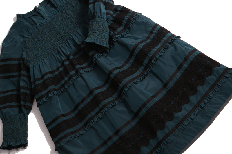 Tealength frock in luxurious Taffeta with elasticized smocking at bust and cuffs, tiers of ribbons and lace trim, invisible zipper at back, long cinched sleeves, and square ruffled neckline. Unlined for lightweight feel. Colour: Celtic and Black, Tia Cibani.