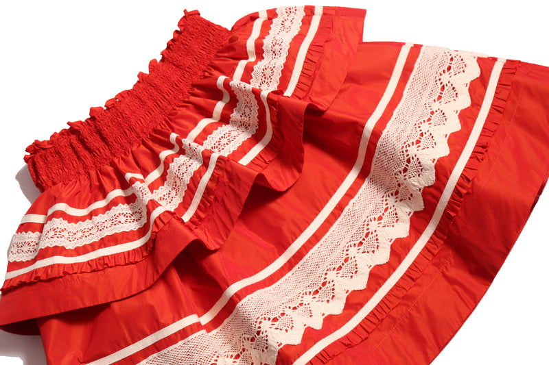 Tealength two-tiered taffeta skirt with elasticized smocking at the waistband, embroidered lace trim, and ribbon at each tier. Unlined for lightweight feel. Colour: Rouge and White, Tia Cibani.