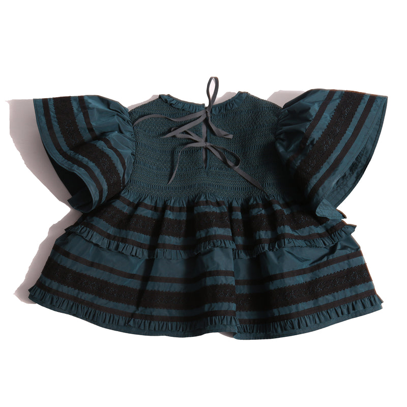 Top in luxurious Taffeta with elasticized smocking at neckline, ruffle detail, and embroidered lace trim and ribbon at body and flutter sleeves. Tonal ribbon ties at the back of the neck. Unlined for lightweight feel. Colour: Celtic and black, Tia Cibani.