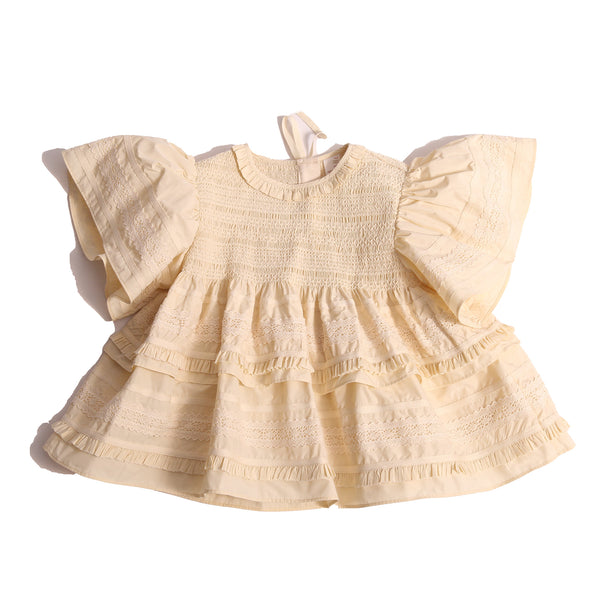 Top in luxurious Taffeta with elasticized smocking at neckline, ruffle detail, and embroidered lace trim and ribbon at body and flutter sleeves. Tonal ribbon ties at the back of the neck. Unlined for lightweight feel. Colour: White, Tia Cibani.