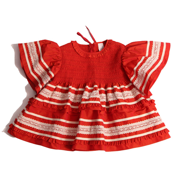 Top in luxurious Taffeta with elasticized smocking at neckline, ruffle detail, and embroidered lace trim and ribbon at body and flutter sleeves. Tonal ribbon ties at the back of the neck. Unlined for lightweight feel. Colour: Rouge and white, Tia Cibani.