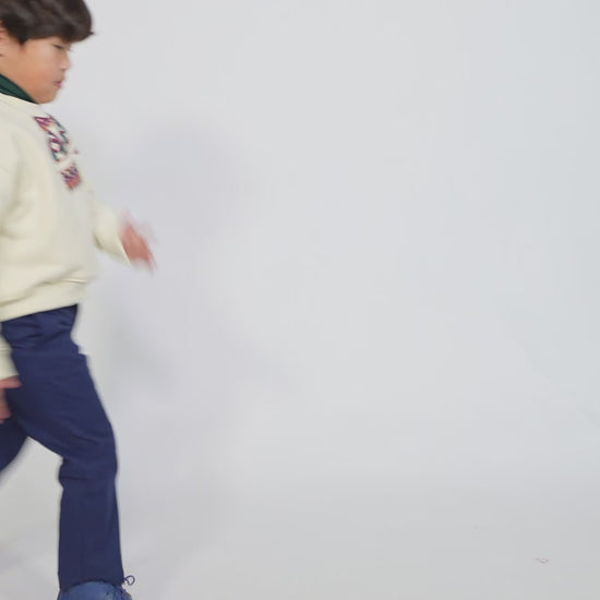 Boy wearing Sueded Fleece jersey pullover for boys, featuring long sleeves, tonal jersey ribbing at neckline, hem, and cuffs for comfort and style. Colorful asymmetric screen print at shoulder. Taffeta pocket detail at left chest for treasures. Dropped shoulders, relaxed fit. White, Tia Cibani.