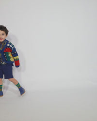 Boy wearing  a colorful fair isle cardigan in a patchwork design, blending various fair isle patterns with solid colors of Felt Wool Yarn. Features a relaxed fit with faux horn buttons at the center front, ideal for layering over basic knits. Made from 100% Wool. Color: Multicolor. By Tia Cibani.