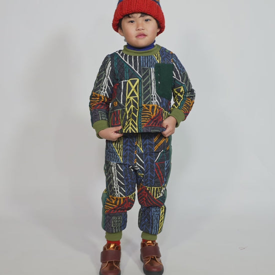 Boy wearing an hand-knitted toque in 100% wool with multi-colored fair isle pattern, large pom pom at top, and ribbing at bottom for easy folding. Colour: Blue and yellow, Tia Cibani.