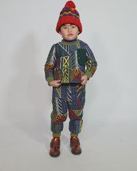 Boy wearing an hand-knitted toque in 100% wool with multi-colored fair isle pattern, large pom pom at top, and ribbing at bottom for easy folding. Colour: Blue and yellow, Tia Cibani.