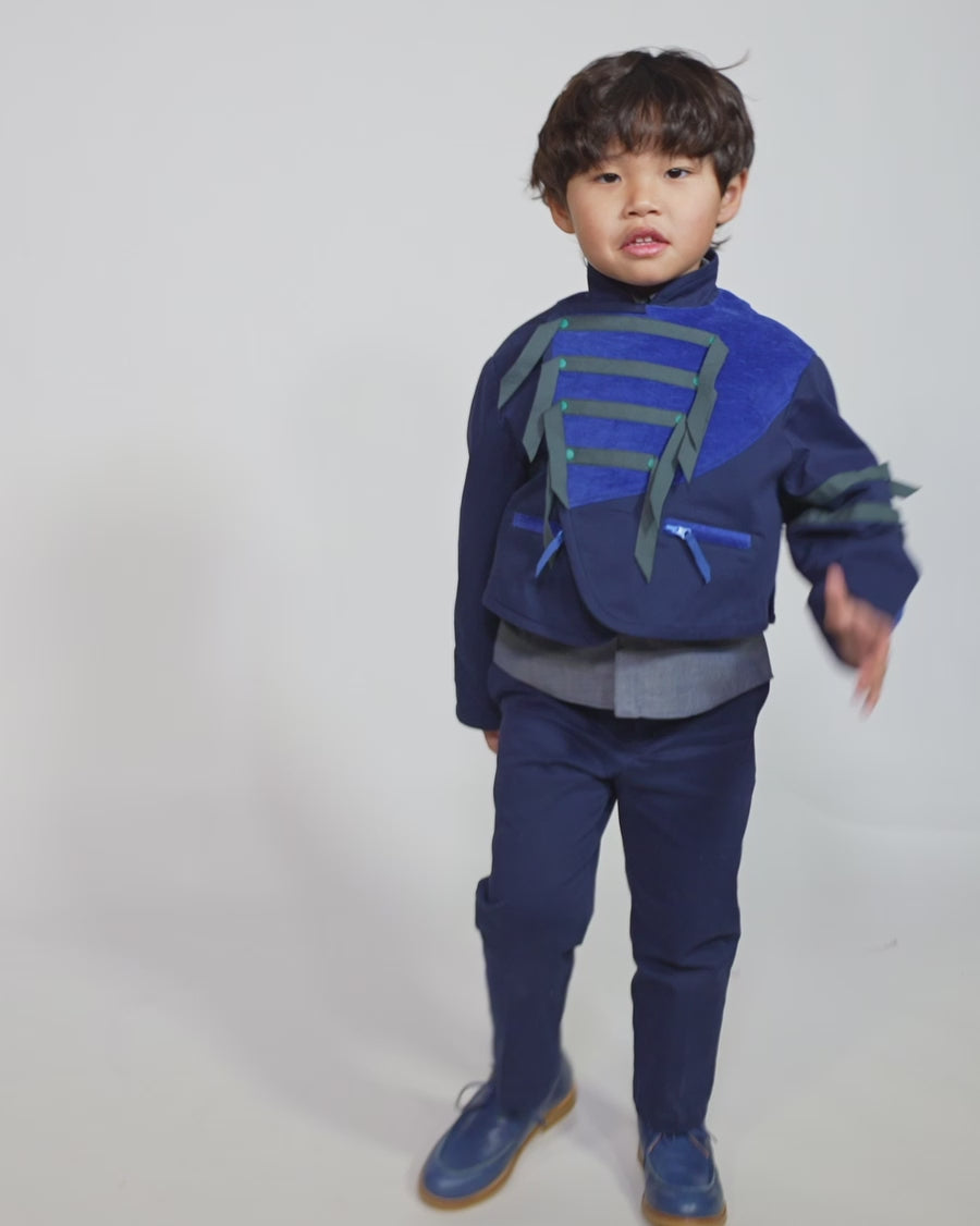 Boy wearing a western-inspired take on classic boy's button-up with scoop high-low hem for modern twist. Built-in vest with two-toned embroidery design and textured ribbons at overlay. Snap closure at center front for easy dressing. Perfect for any occasion, from family gatherings to formal events. Cotton. Blue, Tia Cibani. 