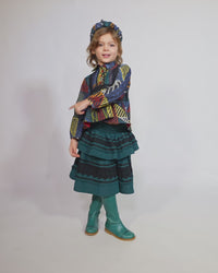 Girl wearing a tealength two-tiered taffeta skirt with elasticized smocking at the waistband, embroidered lace trim, and ribbon at each tier. Unlined for lightweight feel. Colour: Celtic, Tia Cibani.